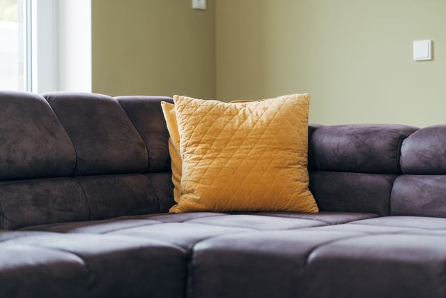 Senfgelbes Kissen auf einem grauen Sofa, Detailaufnahme